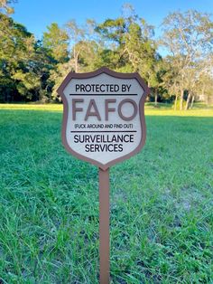 a sign that is in the grass with trees in the backgroung behind it