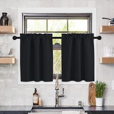 a kitchen window with black curtains in front of the sink and counter top, next to a potted plant