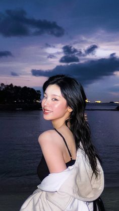 a woman standing in front of the ocean at dusk