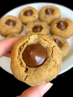 a hand holding a peanut butter cookie with chocolate in the middle on a white plate