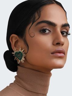 a woman with black hair wearing green earrings and brown turtle neck sweater, looking off to the side