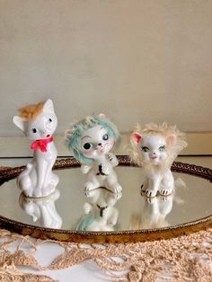 three little white cats sitting on top of a glass table next to each other in front of a mirror