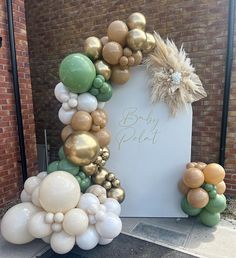 an arch made out of balloons with a baby announcement sign in the middle and gold, white and green balloons