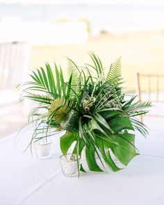 a vase filled with green plants sitting on top of a white table covered in greenery