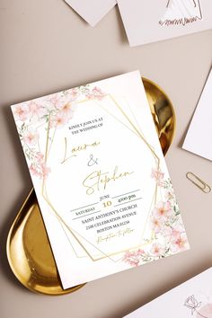 the wedding stationery is laid out on a gold tray with pink flowers and greenery