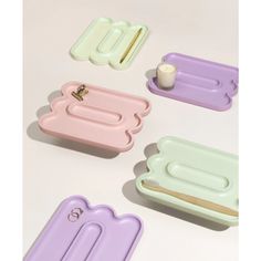 four pastel trays with toothbrushes, soap dish and candle on white surface