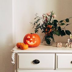 a white dresser with two pumpkins and flowers on it