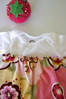 a baby's bodysuit with flowers on it next to a strawberry shaped object