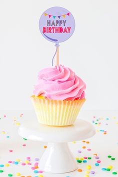 a cupcake with pink frosting and a happy birthday sign on top sitting on a cake stand