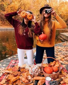 two women standing next to each other on a table covered in leaves and pumpkins