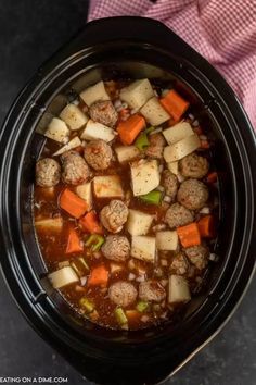 a crock pot filled with meatballs and carrots next to a pink towel