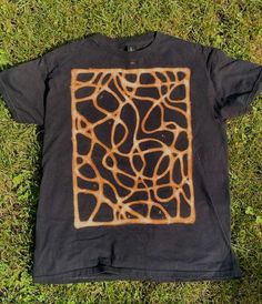 a black t - shirt with an abstract design on the front and back, laying in grass