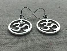 "Stunning silver Ohm round earrings. These are the perfect accessory for any yoga, meditation lover. Bring a little namaste into your life. Made from allergy free plated silver. They measure 5/8\" across by 3/4\" long and hang from simple silver ear wire hooks. I have a matching necklace in my Etsy shop. Here is the link https://etsy.me/2VBdAv9 Thanks for stopping by! Please take a moment and visit the rest of my Etsy shop. I have many more unique and stylish jewelry to choose from. 🌸 Tiger Flo Symbolic Round Earrings For Pierced Ears, Symbolic Round Pierced Earrings, Pierced Symbolic Round Earrings, Symbolic Round Metal Earrings, Nickel-free Symbolic Round Earrings, Symbolic Nickel-free Round Earrings, Symbolic Round Nickel-free Earrings, Ohm Jewelry, Statment Earrings