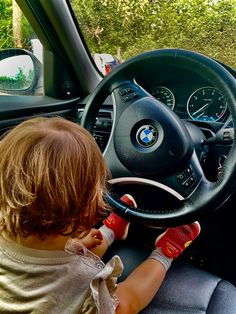 a little boy sitting in the driver's seat of a car with his hands on the steering wheel