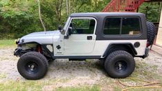 a white jeep parked in front of a wooden structure with trees and bushes behind it