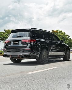 a black suv is parked on the side of the road in front of some trees