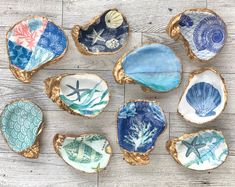 nine seashells with different designs on them sitting on a wooden surface, all painted in blue and green