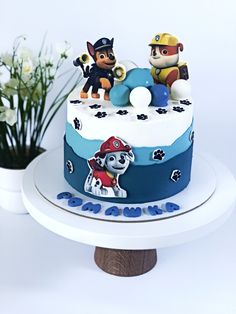 a birthday cake with paw patrol figures on it and flowers in the background for decoration