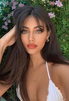 an image of a woman with long hair posing in front of some bushes and flowers