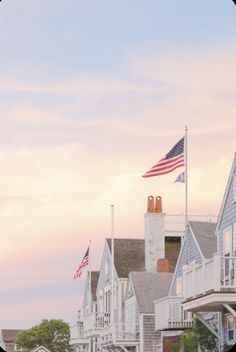 a row of houses with an american flag in the foreground and a pink sky behind them