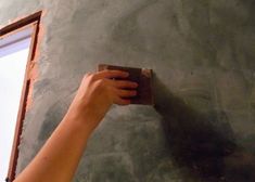 a person is holding up a piece of paper to paint the wall with cement on it