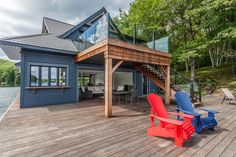 a deck with two chairs and a table on it next to a house near the water