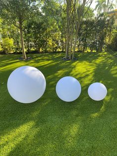 three large white balloons sitting on top of a lush green field