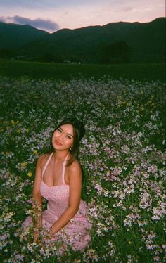 a woman sitting in the middle of a field full of wildflowers at sunset