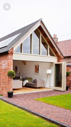 a brick house with an open patio and living room in the back ground, surrounded by lush green grass