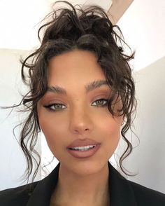 a woman with curly hair wearing a black blazer and gold necklace, posing for the camera