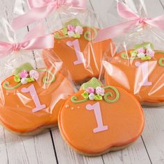 four decorated cookies in plastic bags with pink bows and numbers one on them, sitting on a white wooden surface