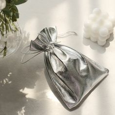 a silver bag sitting on top of a white table next to some flowers and candles