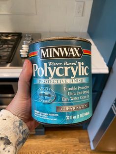 a person holding up a can of polycyclic in their hand, on a kitchen counter