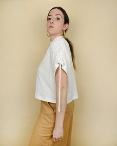 a woman standing in front of a wall wearing a white shirt and tan pants with her hands on her hips