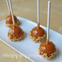 four caramel covered donuts on a white plate with toothpicks sticking out of them