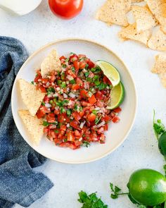 a white plate topped with salsa and tortilla chips next to tomatoes, avocado