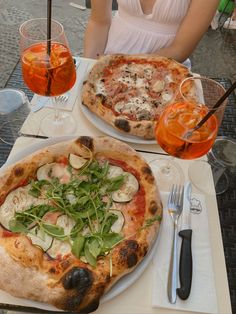 two pizzas sitting on top of a table next to glasses of wine and utensils