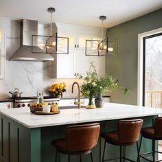 a kitchen with green walls and white counter tops, brown leather bar stools in front of the island