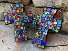 a cross made out of multicolored glass mosaics on a stone wall next to a rock