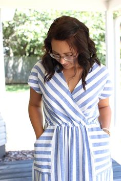 a woman standing on a porch looking down at her cell phone while wearing glasses and a striped dress