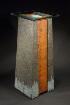 an orange and grey pedestal with glass top on a black background in front of a dark backdrop