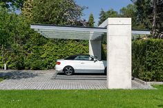 a white car is parked under an awning in a driveway with grass and trees