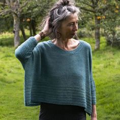 an older woman with grey hair wearing a green sweater and black pants in the park