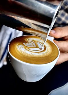 a person is cutting into a latte in a white cup with a large knife