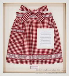 a red and white checkered dress in a wooden frame with a note on it