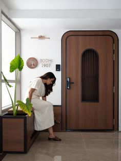 a woman kneeling down next to a potted plant in front of a wooden door