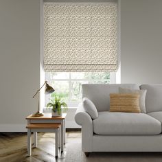 a living room with a couch, coffee table and window covered in roman blind shades