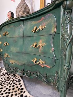 an ornate green dresser with gold knobs on it's doors and drawers, in front of a mirror