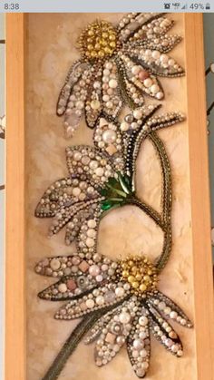 an art piece made out of beads and flowers in a wooden frame on the wall