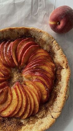 an apple pie on a white table cloth next to a piece of fruit and a knife